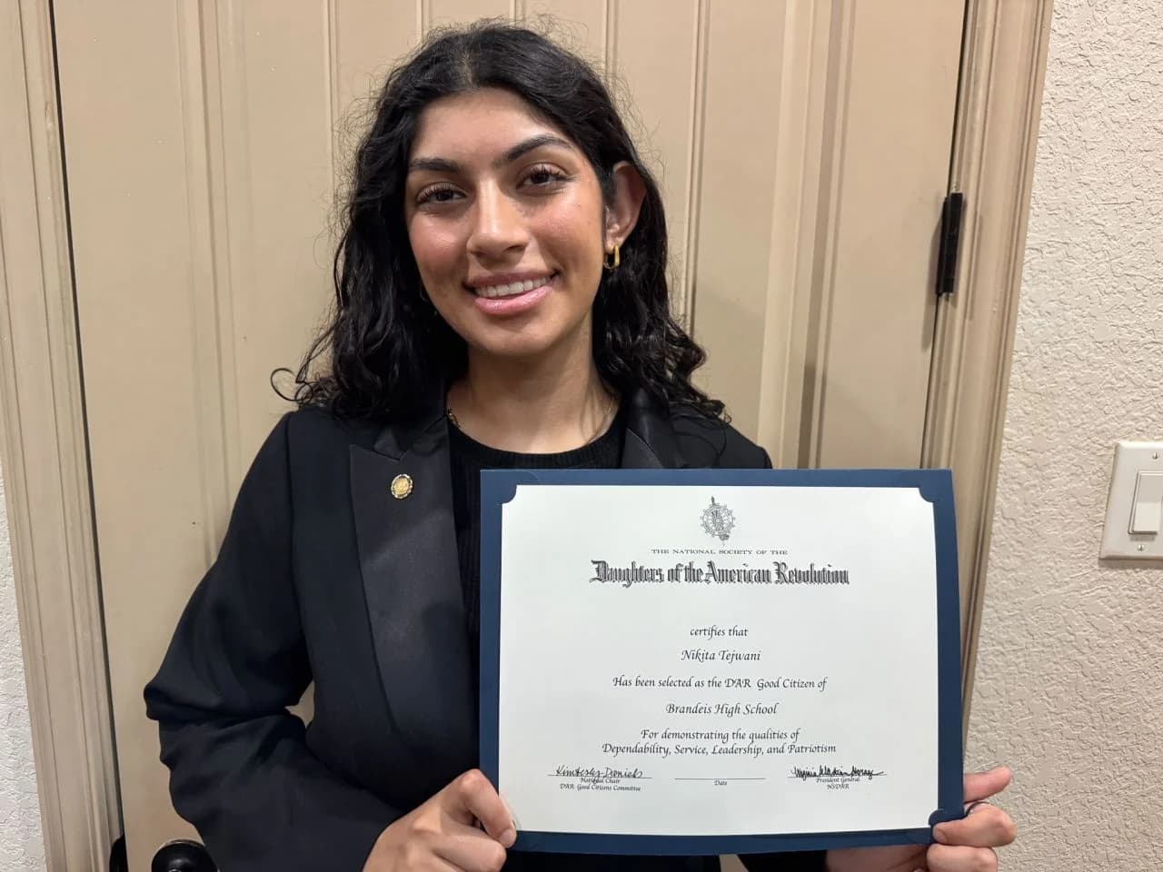 Nikita Tejwani smiling, holding a Daughters of the American Revolution certificate that names her the DAR Good Citizen of Brandeis High School, for dependability, service, leadership and patriotism.
