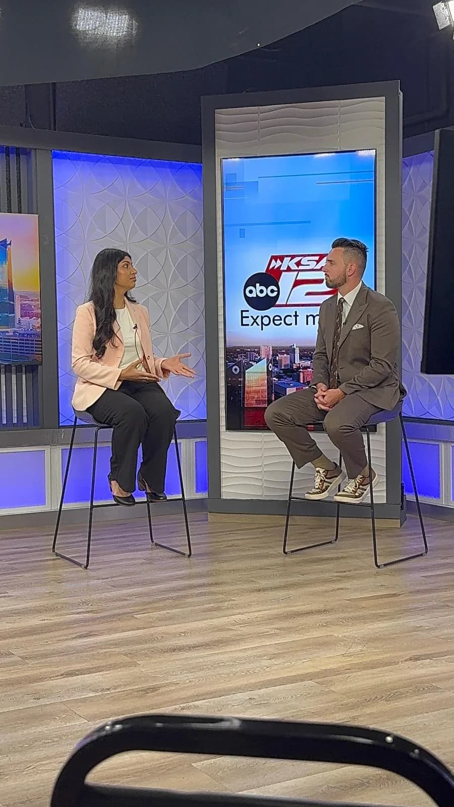 Nikita seated on a stool in the KSAT 12 studio, talking with the show's anchor, who sits across from her in front of a KSAT 12 screen.