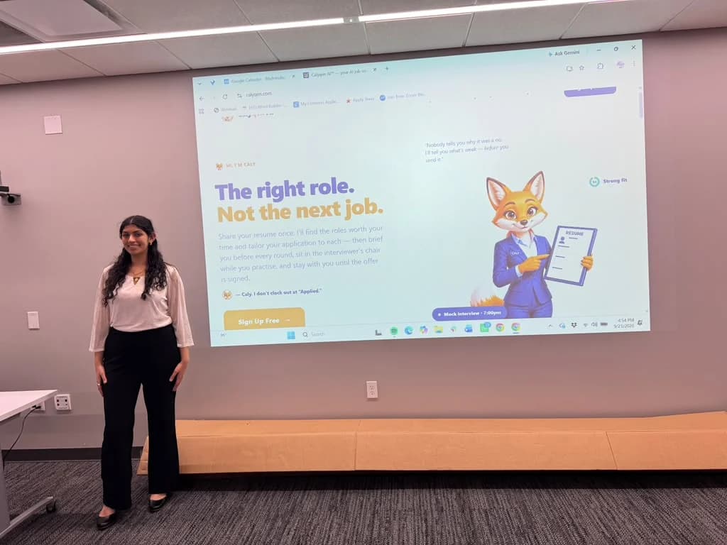 Nikita standing beside a large projected screen showing Calyqen's home page: The right role. Not the next job.