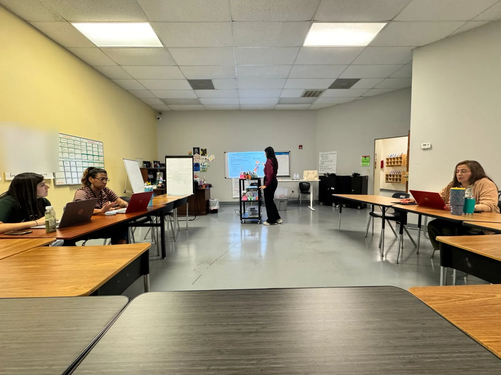 Nikita standing at a projected screen showing Calyqen in an SA Youth classroom, with staff seated at desks working on laptops.