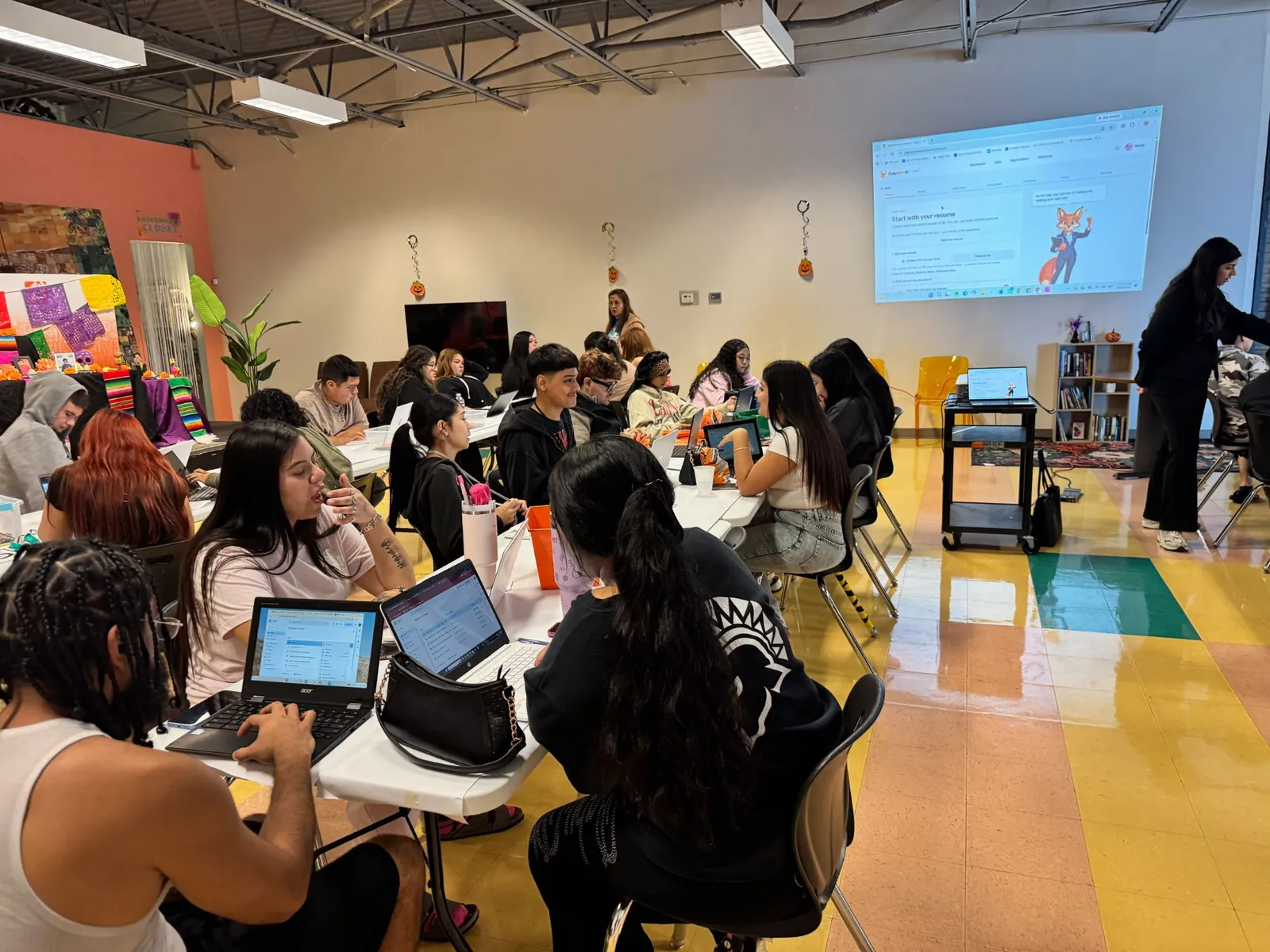 A room of students at tables with laptops, with Calyqen's Start with your resume screen projected on the wall.